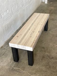 a wooden bench sitting on top of a cement floor next to a white brick wall