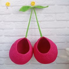 two pink crocheted shoes hanging from a hook on a white brick wall with smiley faces drawn on it