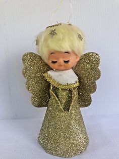 an angel ornament hanging on a white wall with gold glitters and wings