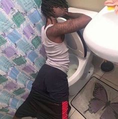 a man with dreadlocks standing in front of a toilet next to a sink