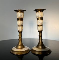 two brass candlesticks sitting on top of a black table next to each other