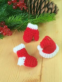 two knitted red and white christmas mittens next to pine cones on a wooden table