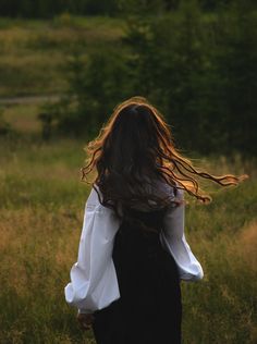 a woman with long hair walking through a field