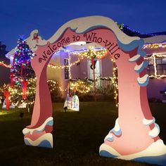 a welcome sign is lit up in front of a house with christmas lights on the trees