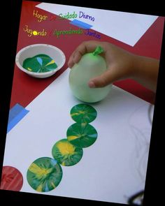 a child's hand is touching a paper plate with green leaves on it while making a caterpillar