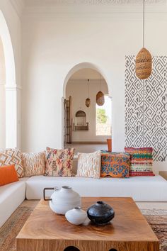 a living room with white couches and colorful pillows on top of the coffee table