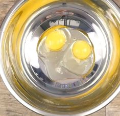 two eggs in a metal bowl on top of a wooden table