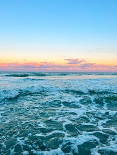 the ocean with waves coming in to shore at sunset or dawn, as seen from an empty beach