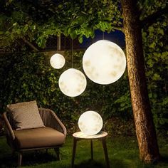 some lights that are on in the grass next to a chair and table with pillows