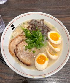 a bowl filled with meat and eggs on top of a wooden table next to a glass of water