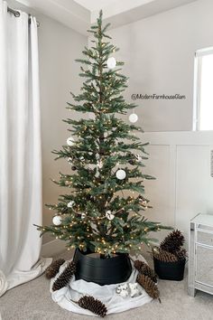 a small christmas tree in a pot with pine cones on the floor next to it