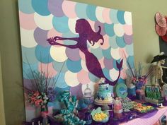 there is a mermaid party table with cake, candy and decorations on the table top