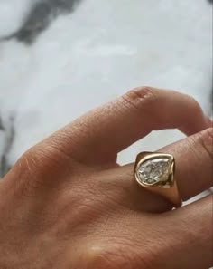 a person's hand with a gold ring on it and a white marble background