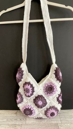 a crocheted bag hanging on a hanger next to a black wall with white and purple flowers