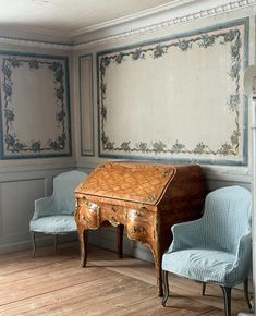 an old desk and two chairs in a room with blue wallpaper on the walls