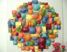 a wall hanging made out of different colored balls and circles with flowers in the foreground