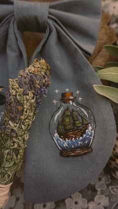 a small glass bottle filled with purple flowers on top of a blue cloth bag next to a plant