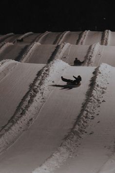 two snowboarders sliding down a snowy hill at night