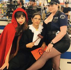 three women dressed up in costumes posing for a photo at a store with police officers behind them