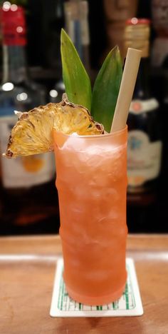 an orange drink with a pineapple garnish on the rim, sitting on a bar