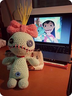 a crocheted stuffed animal sitting next to a laptop computer on a wooden desk