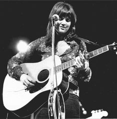 a woman holding a guitar and singing into a microphone