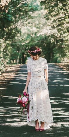 a woman is walking down the road with flowers in her hair and wearing a white dress