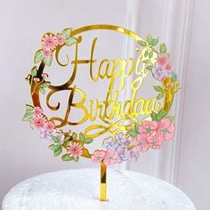 a happy birthday cake topper with flowers and leaves on it, sitting on a white surface