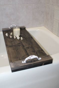 a bath tub with a wooden tray on top of it next to a candle and some flowers