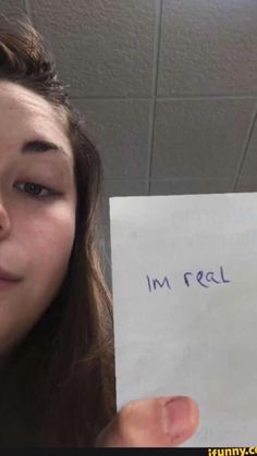 a woman holding up a piece of paper with the words i'm real written on it