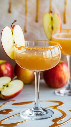 two glasses filled with an apple cider next to apples and caramel drizzle