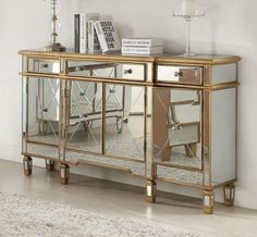 a gold mirrored cabinet with two drawers and three mirrors on the front, along with a white rug