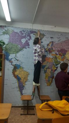 a person standing on a stool in front of a wall with a world map painted on it