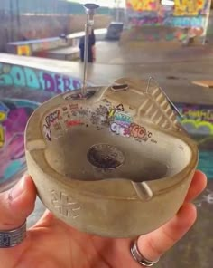 someone is holding an old metal object with graffiti on the wall behind it and in the background there are other skateboard ramps