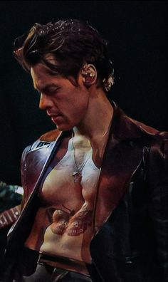 a man with no shirt on holding a guitar and looking at his earrings