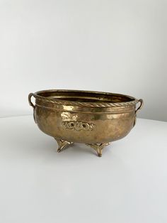 an antique brass bowl with handles on a white surface, possibly used as a planter