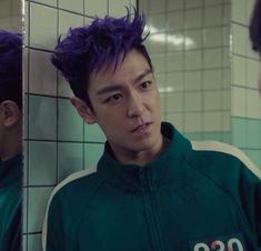 a young man with purple hair standing in front of a mirror looking at his reflection