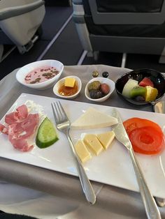 an airplane tray with several different types of food on it, including cheese, tomatoes, cucumbers and olives