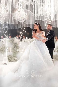 a man and woman in formal wear standing next to each other under a chandelier