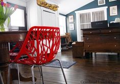 a red chair sitting on top of a hard wood floor next to a wooden dresser