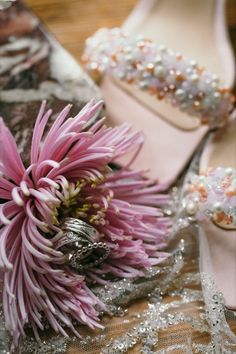 a pink flower sitting on top of a table next to a pair of high heel shoes