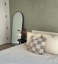 a bed with white sheets and pillows next to a large mirror on the wall above it