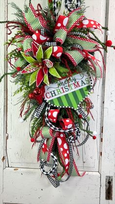 a christmas wreath hanging on the side of a white door with red and green ribbons