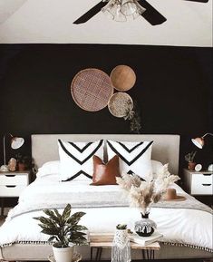 a bedroom with black walls, white bedding and two planters on the nightstands