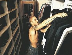 a man with tattoos on his arm is looking at some clothes in a closet,