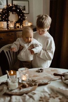 two children sitting at a table with candles in front of them and one holding the baby