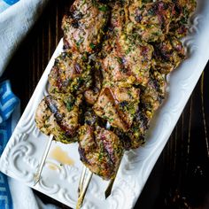 grilled meat on skewers with herbs and seasoning sitting on a white platter