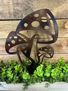 a metal sculpture sitting on top of a planter filled with green plants next to a wooden wall