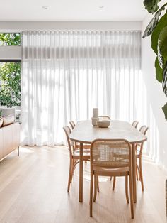 a dining room table and chairs in front of a large window with sheered curtains