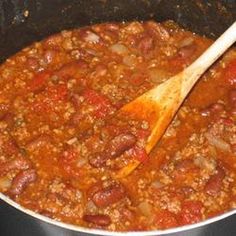 a pot filled with chili and beans next to a wooden spoon on top of a stove